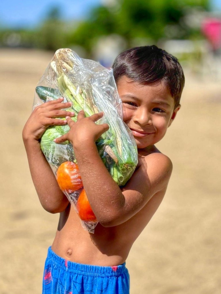 A smiling child holding a bag of fresh vegetables from Grow Pescadero