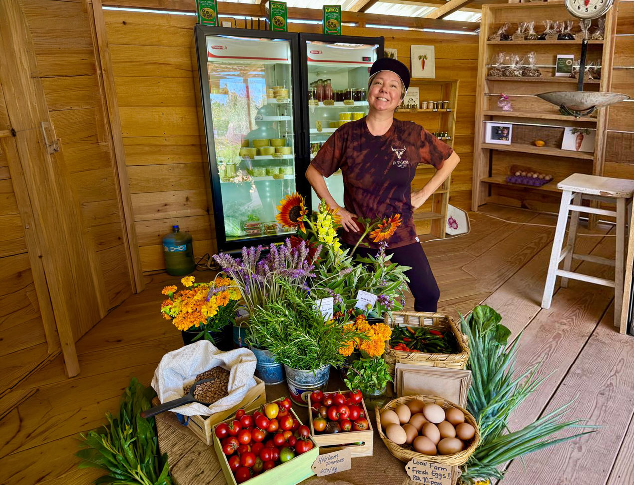 A woman standing behind The Farm Stand produce and flower display