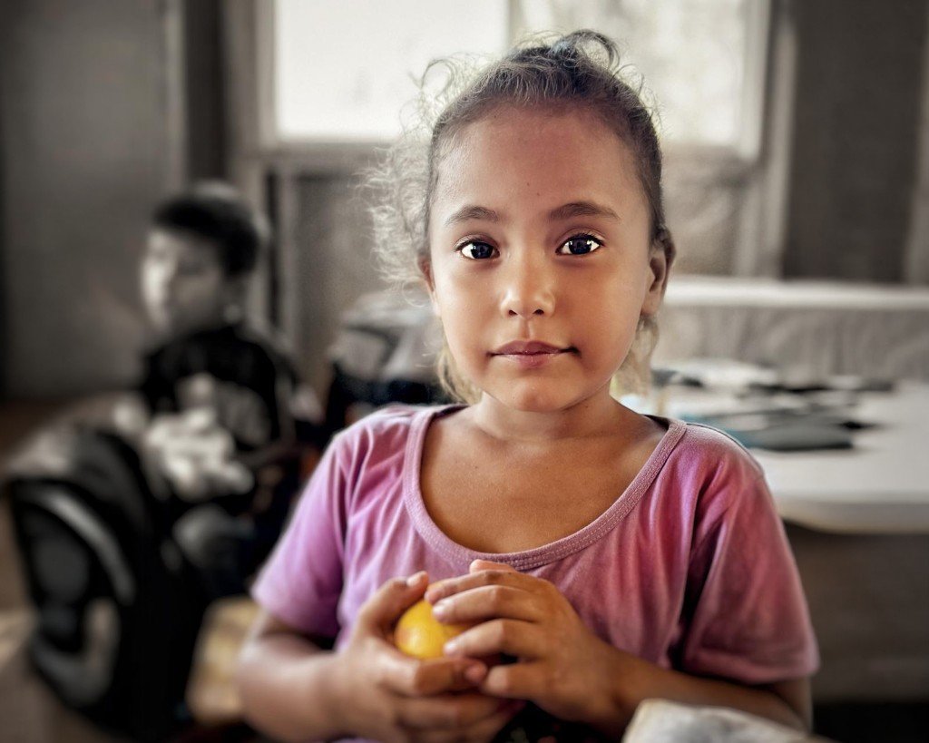 A young girl holding fruit, looking toward the camera